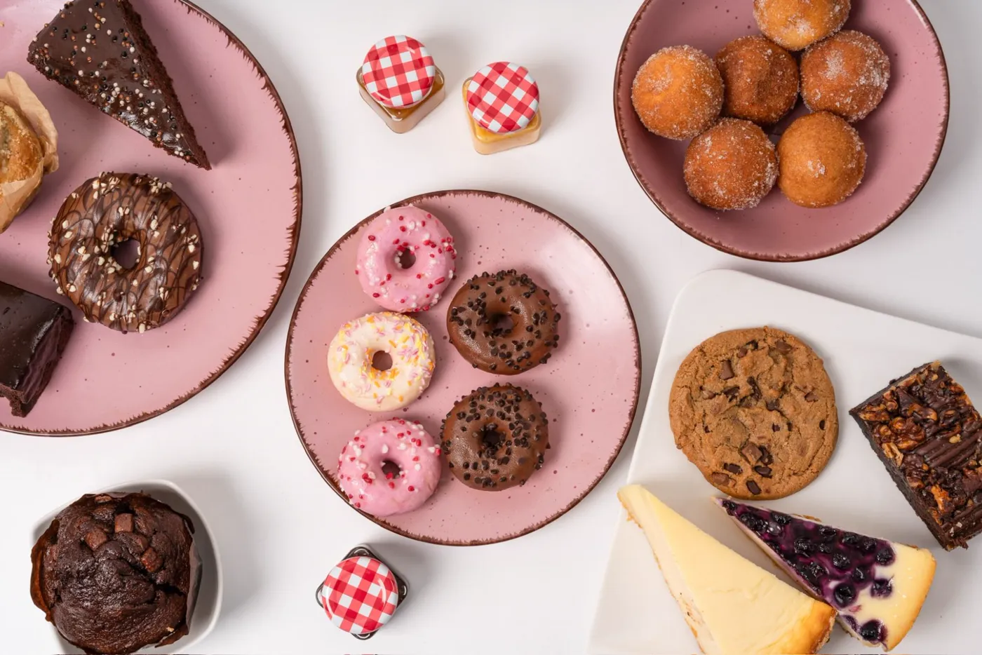 Draufsicht auf Donuts, Quarkbällchen, Cookie, Cheesecakes, Brownies und Muffins auf rosa Tellern
